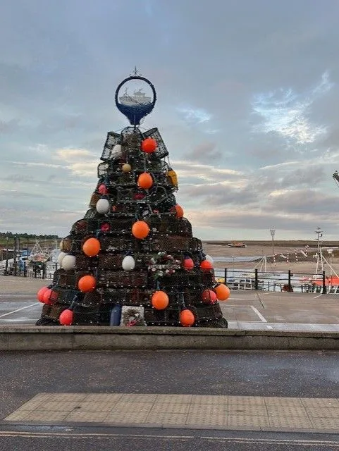 Christmas tree on the quayside at Wells-next-the-Sea, with a dark sky and the harbour behind it