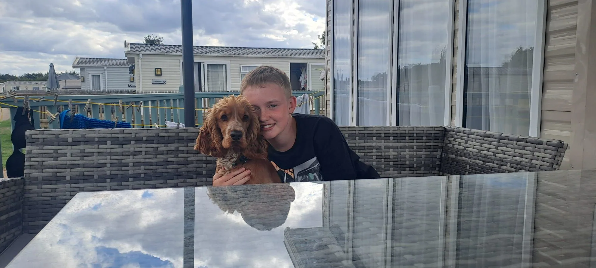 A guest sitting on the deck sofa at Tern 32 with a ginger cocker spaniel, turquoise railings and caravans behind