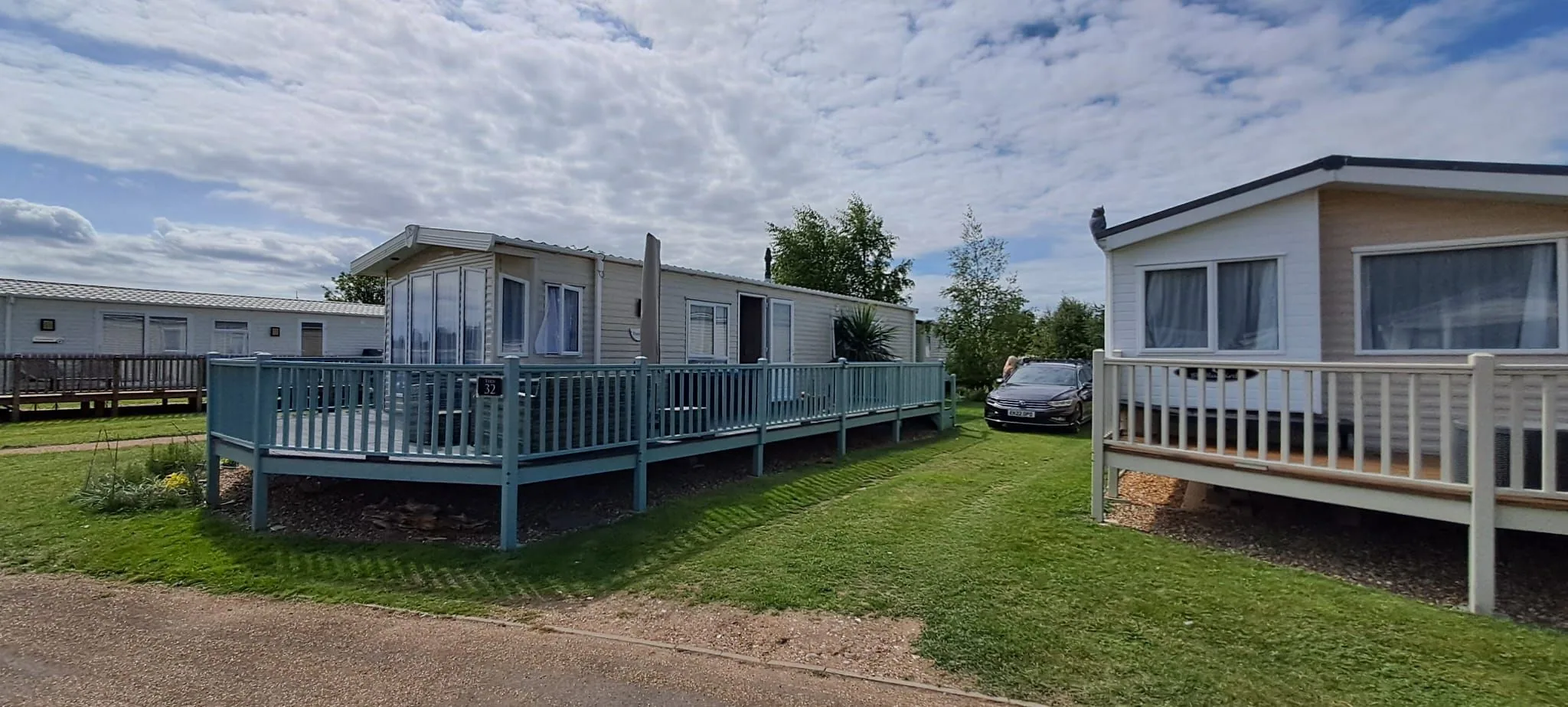 Tern 32 with its turquoise deck and railings on a grassy plot, with a car beside it and other caravans around