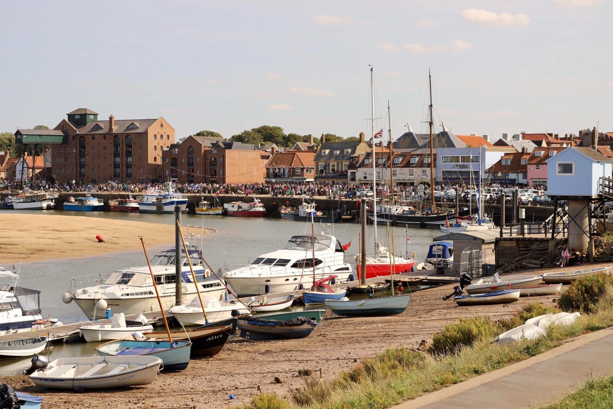 Wells quayside on a summer day with crowds, moored boats and brick buildings behind