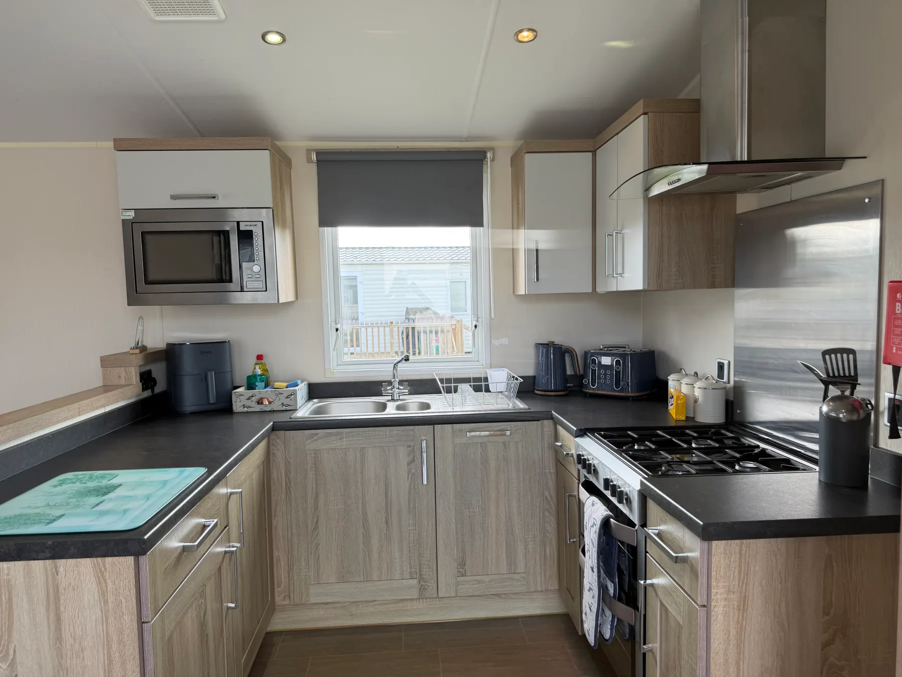 Kitchen inside Tern 32 with light wood and white units, a black worktop, double sink, built-in microwave, gas hob and extractor hood