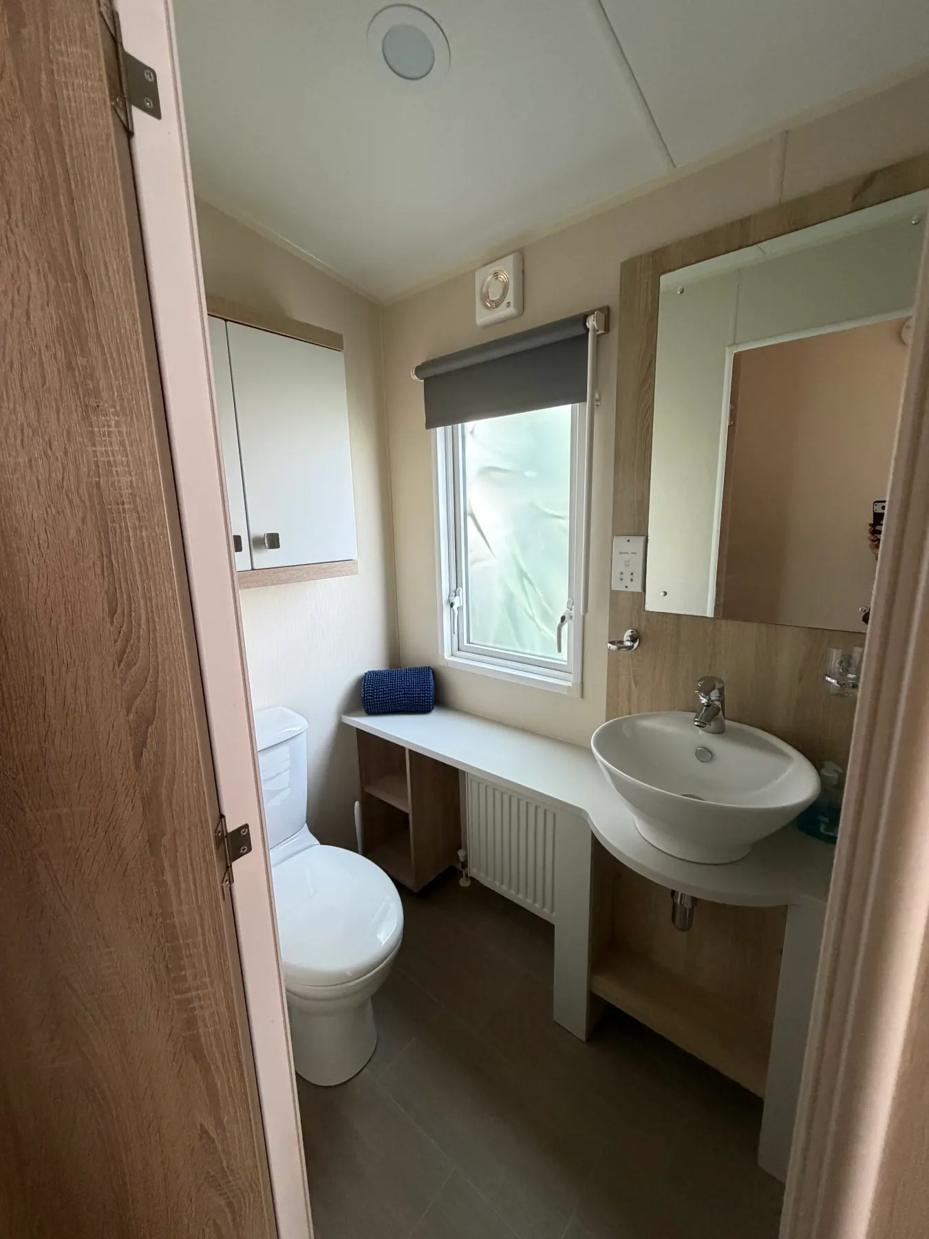 Shower room and bathroom inside Tern 32 with a white toilet, round basin on a wooden vanity, mirror, frosted window and towel rail