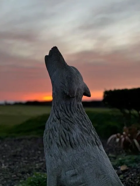 A stone statue of a howling dog or wolf silhouetted against a sunset