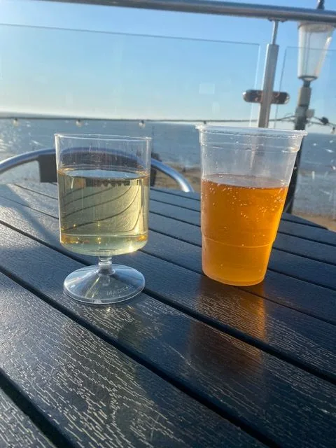 Two drinks on a dark table on a seafront terrace, with the sea and a pier behind