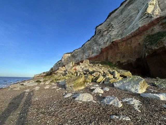 The striped chalk and red cliffs at Hunstanton seen from the beach, with grey rocks and shingle in the foreground
