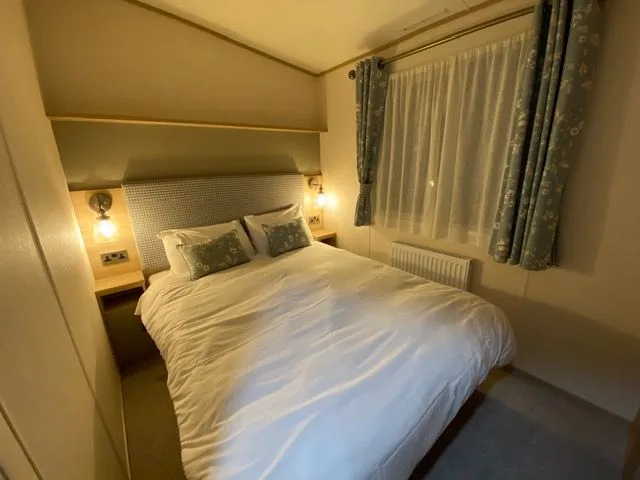 The double bedroom inside Windsor 30 with a double bed, upholstered headboard, bedside lights and patterned curtains