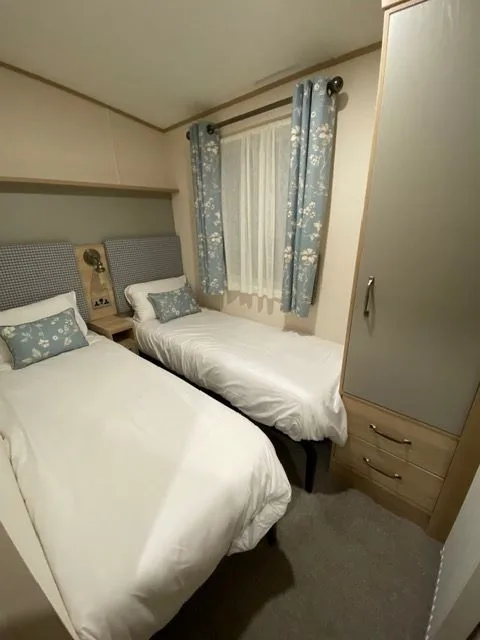A twin bedroom inside Windsor 30 with two single beds, white bedding, blue floral cushions and a wardrobe with drawers